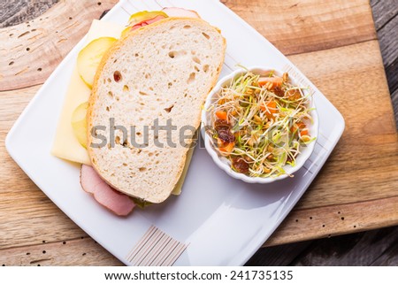 Sandwich with ham, cheese, pickled cucumber and fresh sprouts salad on old wooden table