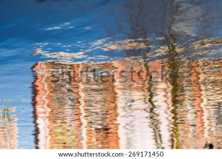 close up of water surface with ripples. sky with clouds, building or tree reflected in water.