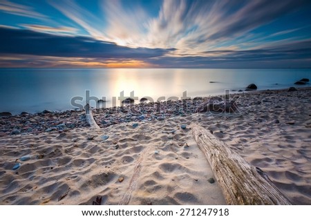 Beautiful rocky sea shore with driftwood trees trunks at sunrise or sunset. Baltic sea shore