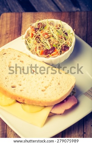 Vintage photo of sandwich with ham, cheese, pickled cucumber and fresh sprouts salad on old wooden table