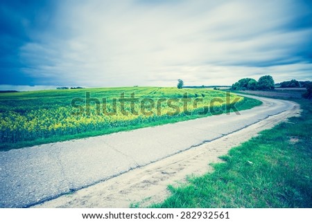 Vintage photo of rural asphalt road near fields in springtime. Calm polish countryside