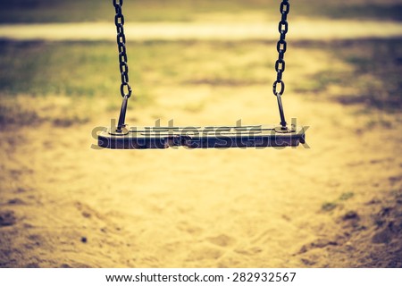 Vintage photo of empty swing on children playground in city. Old fashioned colors photography.
