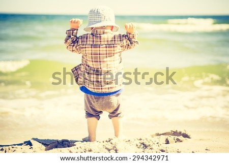Little child playing on sea shore at good summer weather. Photo with vintage mood effect