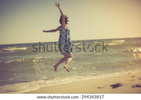 Woman jumping in water on sea shore with her legs in water. Summertime photo with vintage mood effect