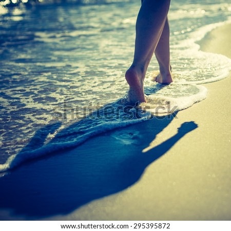 Vintage photo of woman\'s legs walking by sea shore. Close up of sea shore with woman walking through waves.