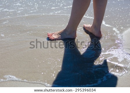 Woman legs walking by sea shore. Close up of sea shore with woman walking through waves.