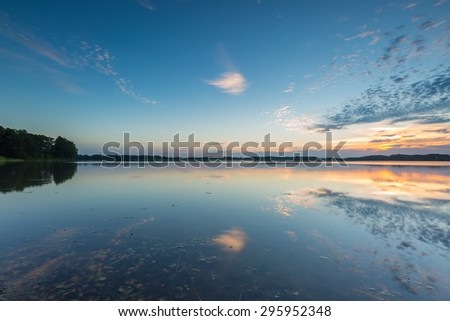Beautiful lake at sunset landscape with cloudy sky reflecting in water. Polish lake in Mazury lake district