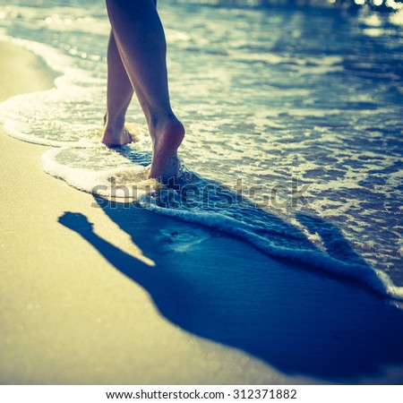 Vintage photo of woman\'s legs walking by sea shore. Close up of sea shore with woman walking through waves.