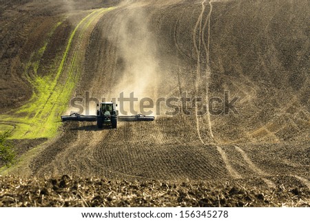 plowed land on a farm in the background with farm tractor