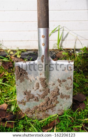 dirty garden spade stuck in the ground on a white wooden background