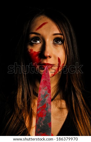 closeup portrait of sweet and innocent woman with bloody knife in her hand in the dark