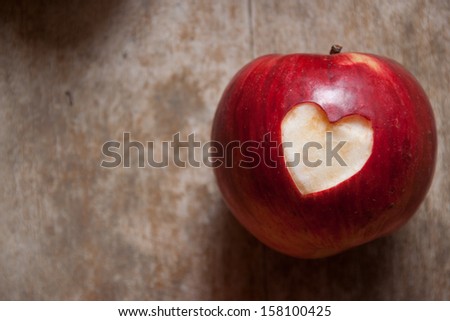 Ripe red apple with a heart shape neatly cut of the skin on a textured weathered wooden surface