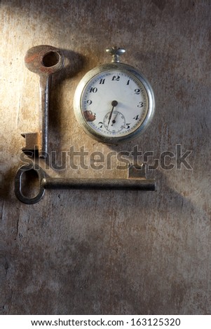 Pocket-watch and rusty keys on wooden texture background.
