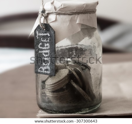 budget concept, chalk inscription, glass bank with many world coins and budget word or label on saving money jar, toned