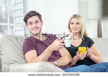 Happy Friends have fun together. Cheerful young people sitting on the couch and drinking tea or coffee while cuddling fun and make self on the tablet. People keep smiling and laughing with tablet