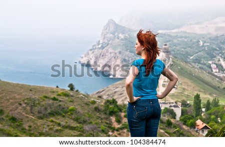 a young girl stands among the mountains and watching a beautiful sea view