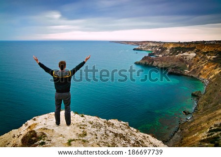 young man stands on a hill with raised hands