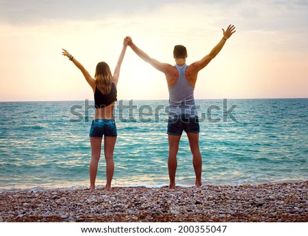 Young couple near the sea at sunset with arms raised