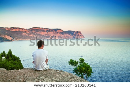 young man sitting on a hill and looking over the sea