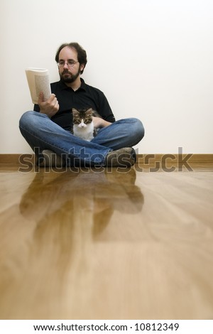 man siting on the floor with his cat while reading a book