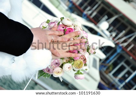 Hands of just married on wedding bouquet with the sea and yacht in background