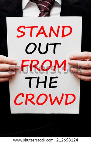 Stand out from the crowd concept. Businessman wearing black suit holding in his hands a paper with a business message text wording on it.