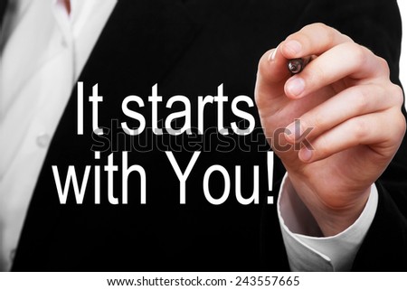 It Starts With You! Businessman or teacher writing a motivational message text on transparent glass
