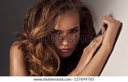 Glamour portrait of young beautiful woman with evening makeup, looking straight with hands based on the wall