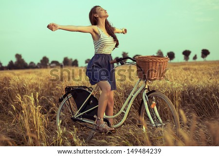Free woman enjoying freedom on bike on wheat field at sunset
