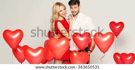 Fashionable couple with balloons heart hugging at each other