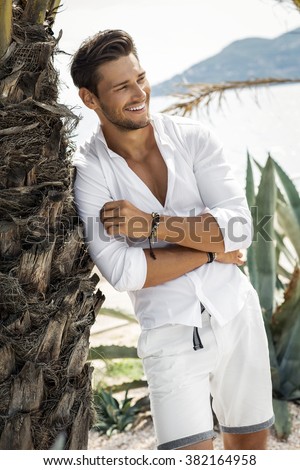 Cheerful smiling young male model wearing white shirt in summer scenery