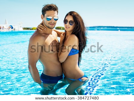 Attractive young couple in swimming pool wearing sunglasses and hugging at each other