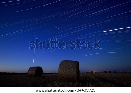 Hay bale at night with star trails in the sky.Star movement is caused by Earth\'s rotation and camera\'s long exposure.