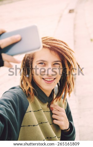 portrait of young guy outdoor with rasta hair smiling with smart phone in a lifestyle concept with a warm filter applied