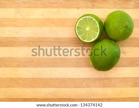 green  lemons sit on a worn butcher block cutting board