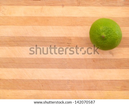 Green lemon sit on a worn butcher block cutting board