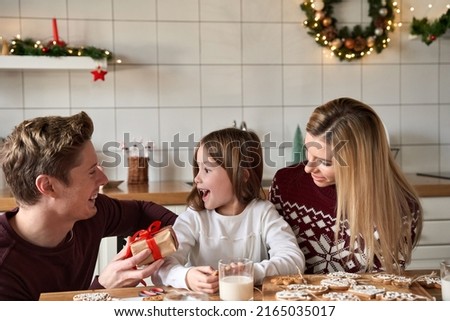 Dad presenting gift box to excited kid daughter at home. Happy father making present greeting cute small child girl with xmas gift sitting at kitchen table celebrating Christmas family holiday.