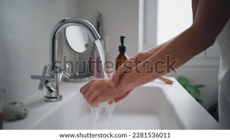 Girl washing hands at bathroom sink closeup. Unknown woman rubbing fingers under faucet at ceramics wash basin. Young lady cleaning arms alone at light modern apartment. Basic home hygiene concept