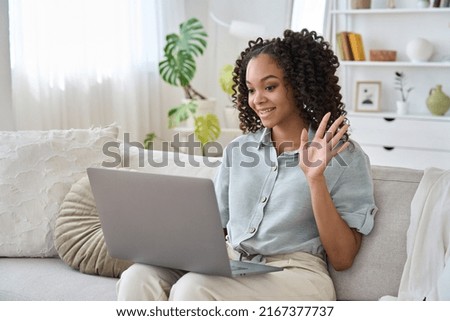 Happy African teen girl waving using laptop computer enjoying online virtual chat video call with friends or family in distance e chat virtual meeting using laptop computer sitting on sofa at home.