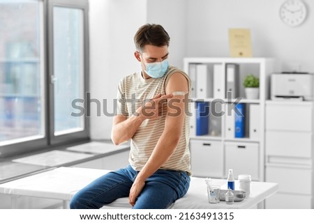 health, medicine and pandemic concept - male patient in mask showing patch on his arm after vaccination at hospital