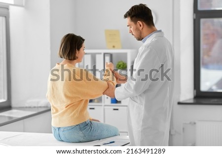 medicine, healthcare and people concept - male doctor with clipboard talking to woman showing her sore arm patient at hospital