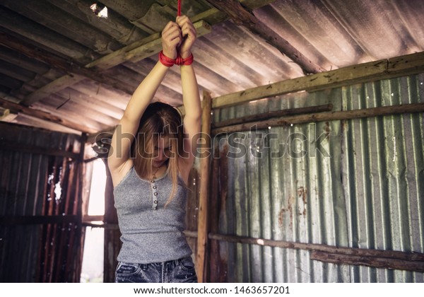 Sad Asian Hostage Woman Tied Hands With Red Rope On Dirty Roof Ceiling In Abandoned Room