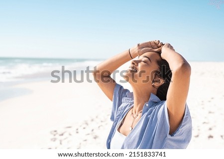 Smiling mixed race woman with eyes closed relaxing on beach. Beautiful young latin woman relaxing at seashore during summer. Happy carefree girl standing on the beach with white sand and copy space.