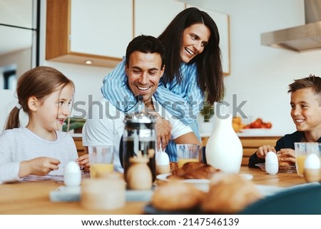 Young family laughing together while eating a healthy breakfast around their kitchen table at home in the morning
