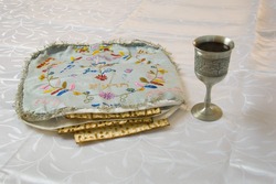 matzo inside an antique embroidered matzo cover for the passover seder, next to a kiddush cup of wine.