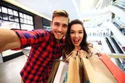 sale, consumerism and people concept - happy young couple with shopping bags walking in mall