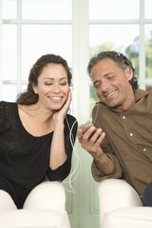Mature couple sharing earphones while listening to music with an mp4 in their home's living room.