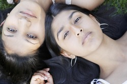 Over head view of two indian girls laying down on grass with their heads together.