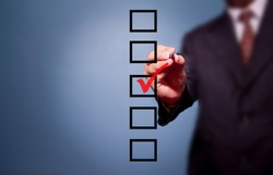Young business man drawing a tick on a glass window in an office. Man choosing one of three options. On a gray background