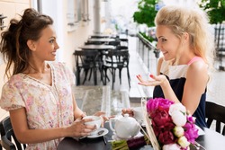 Two young women with great smile and hairstyle sitting at a bar, drinking tea and coffee.